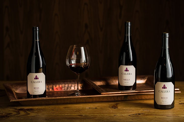 Three bottles of Calera and wine in glass on table